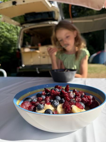A vibrant fruit bowl, filled with bananas, blueberries, and dried cranberries, sits on a white table in the foreground